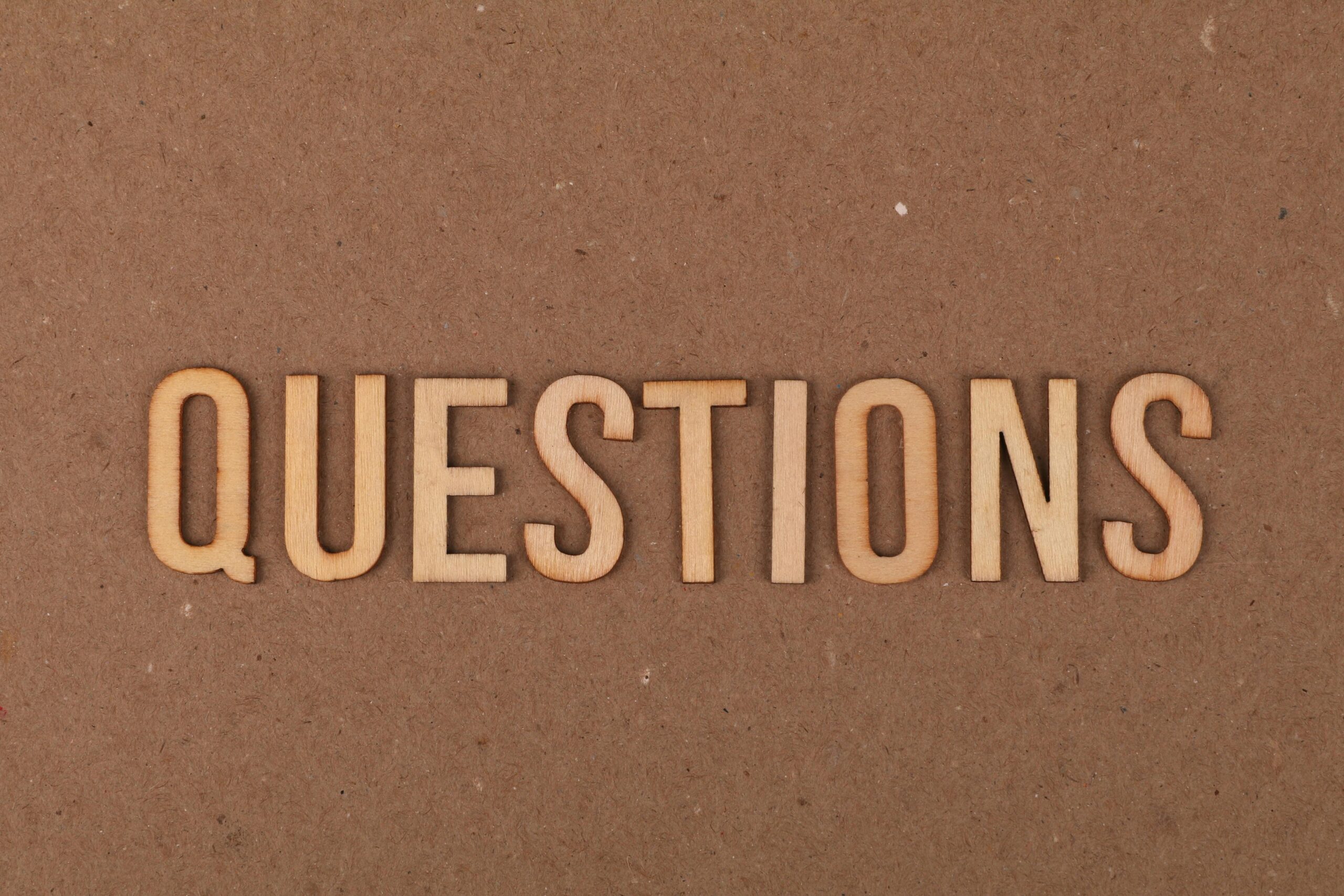 Wooden letters spelling the word "QUESTIONS" on a cardboard background, providing a neutral copyspace.