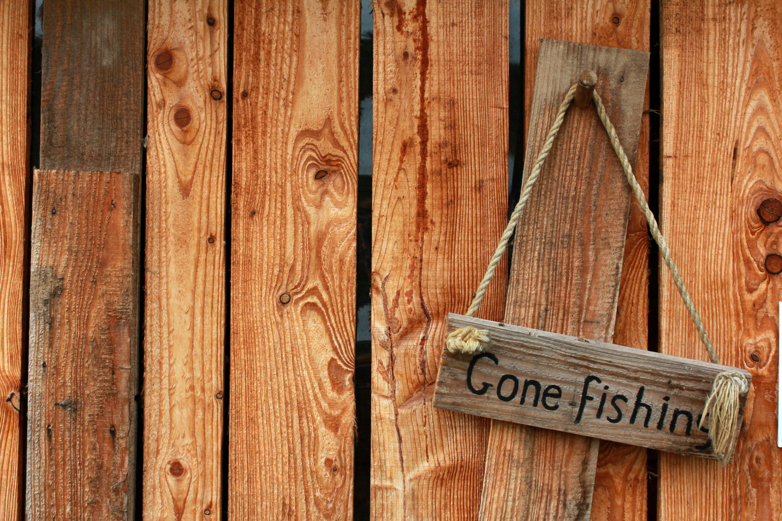 Wooden fence with a rustic 'Gone Fishing' sign hanging, perfect for outdoor and rustic decor themes.