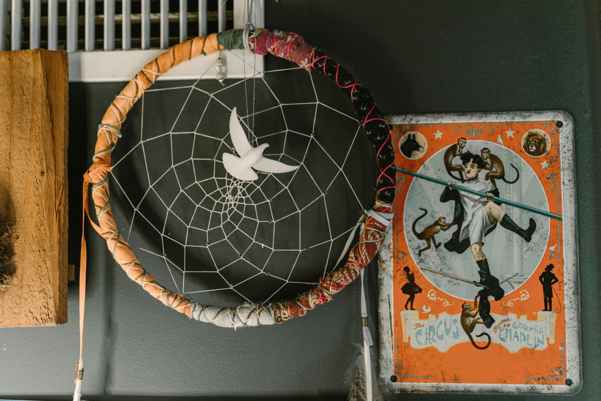 Close-up of dream catcher and vintage circus poster on a gray wall, featuring a unique decorative setup.